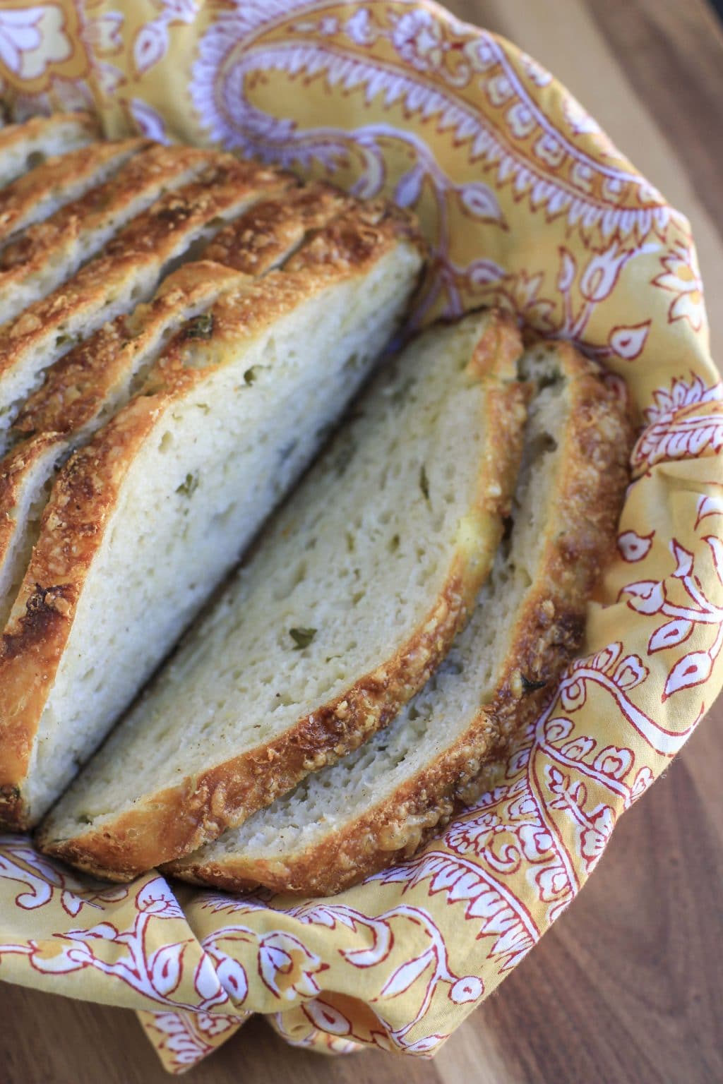 Slices of bread in a basket lined with a yellow paisley napkin on a wooden cutting board.