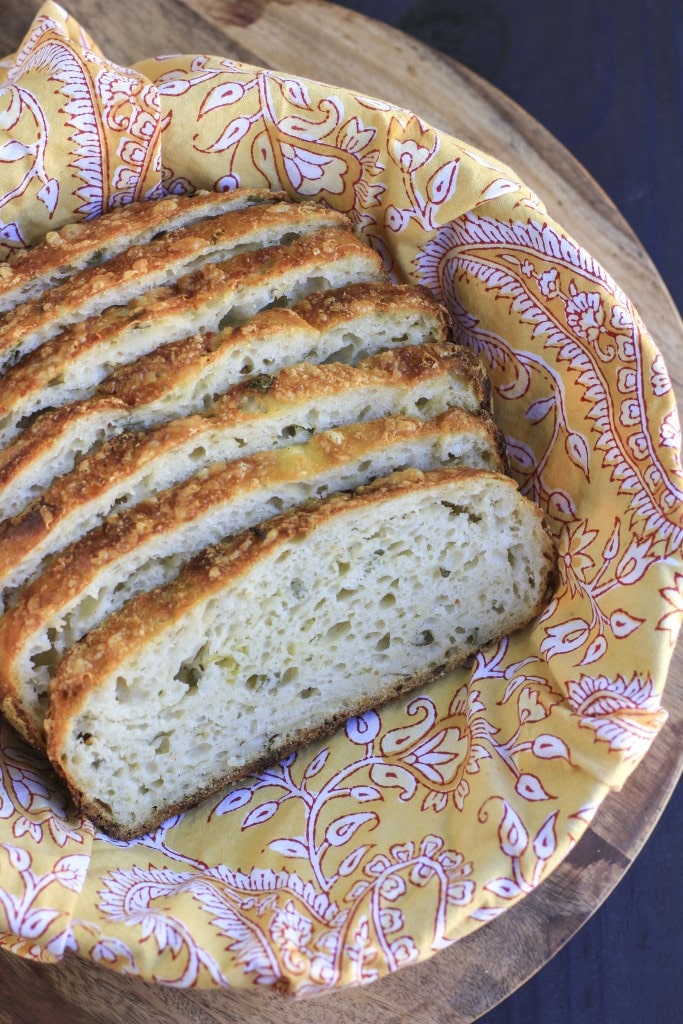 Slices of vegan cheese bread in a basket lined with a yellow paisley napkin on a wooden platter.