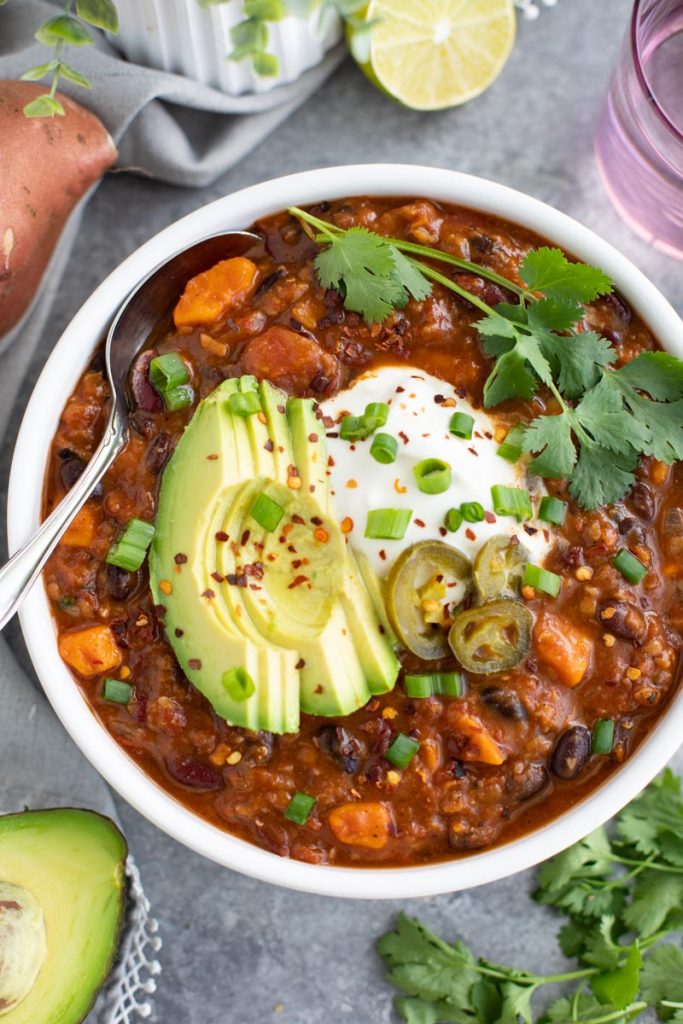 A white bowl filled with vegan sweet potato chili and a spoon dipping into the bowl.