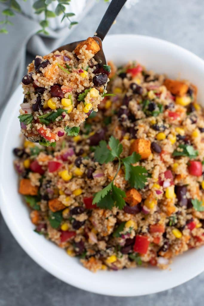 A white bowl filled with quinoa, vegetables, and cilantro on a gray background.