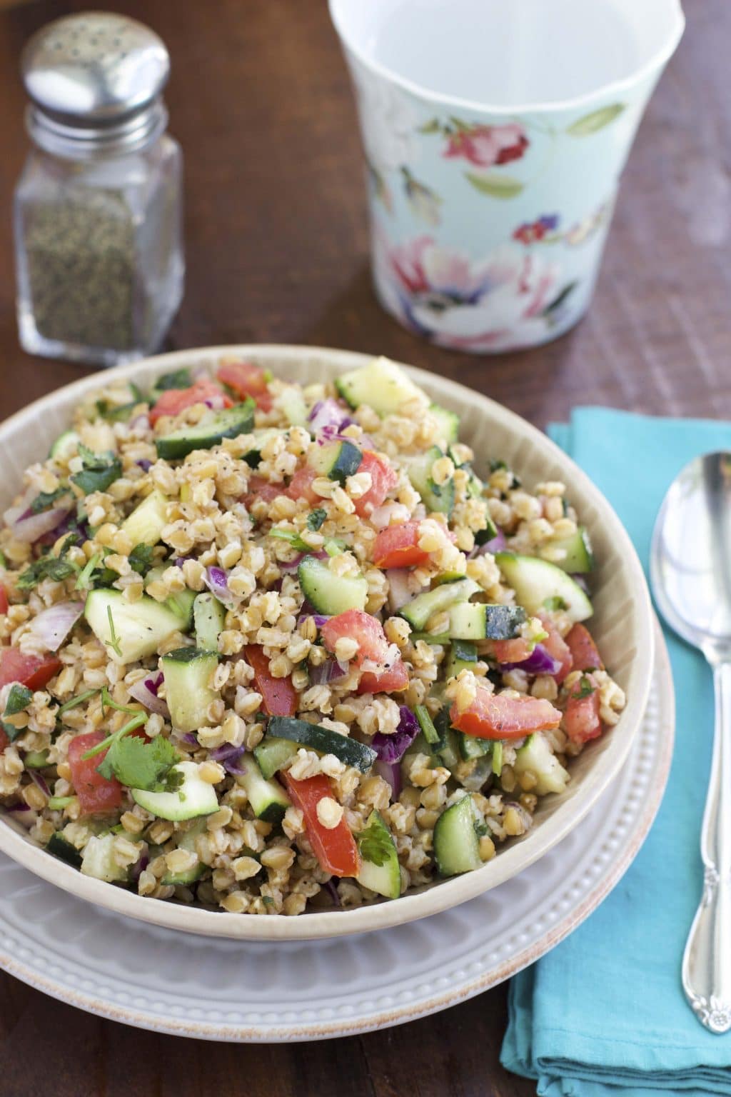 A white bowl filled with wheat berry salad next to a blue napkin. 