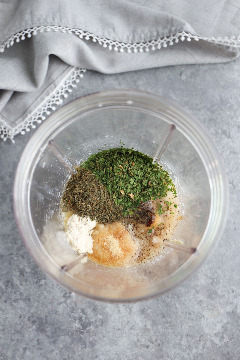 A nutribullet blender cup filled with ingredients to make the dressing next to a gray napkin on a gray background. 