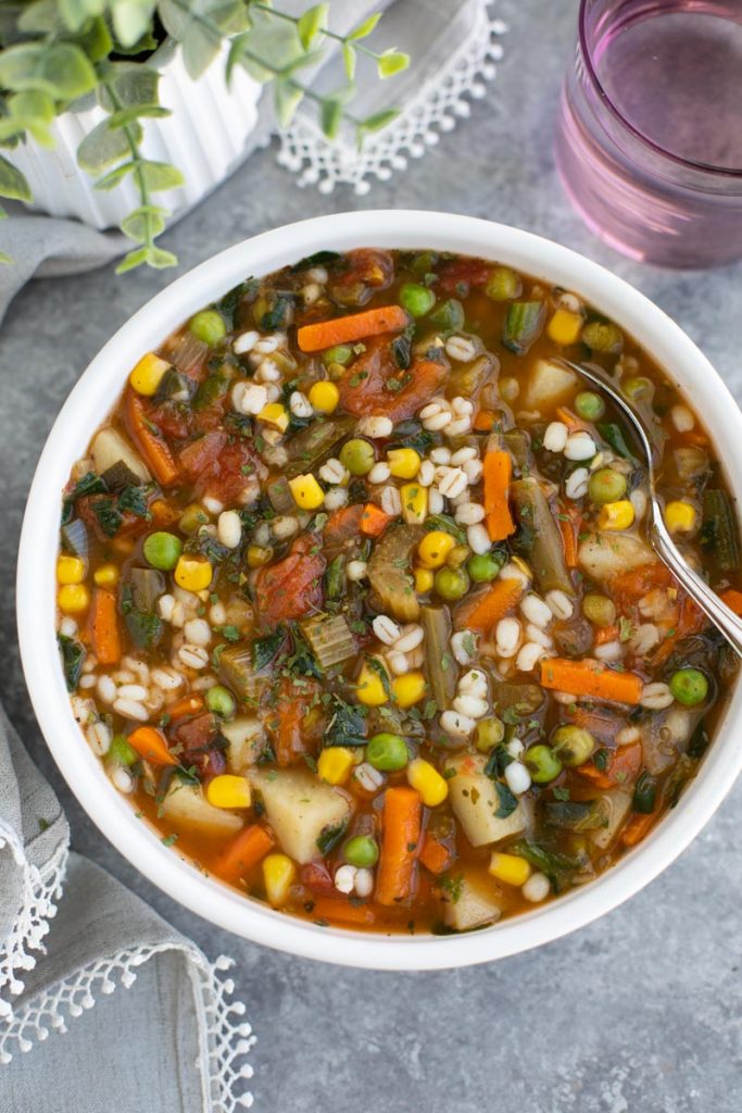A green pot filled with vegan vegetable barley soup on a rustic background. 