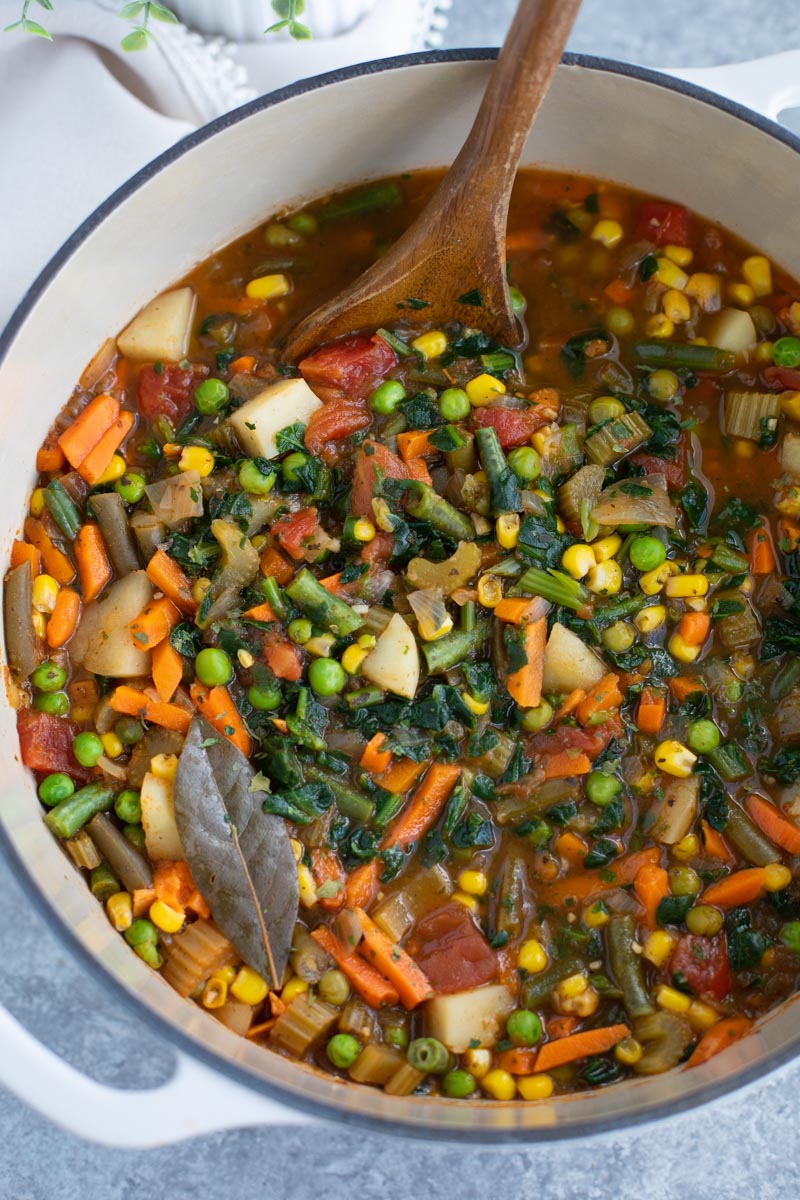 A wooden spoon in a bowl filled with vegetables on a gray background.