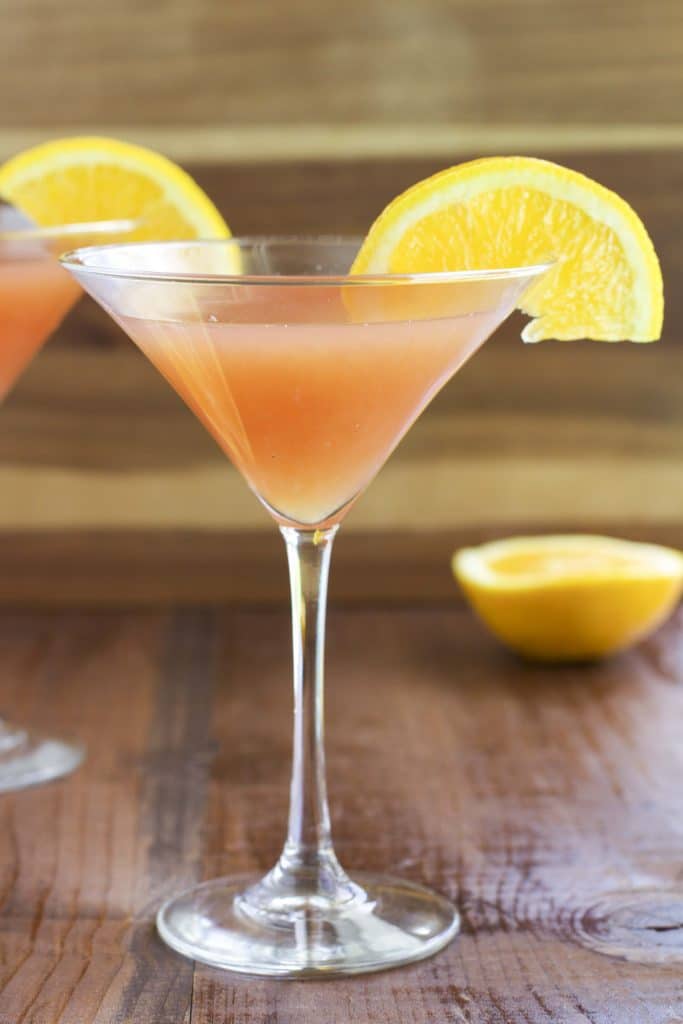 A filled martini glass topped with an orange slice on a wooden table top.