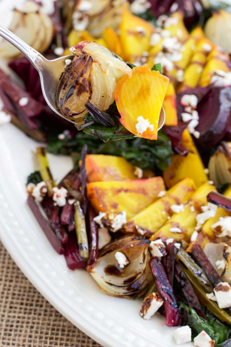 A spoonful of beets held over a large platter filled with beets and onions. 