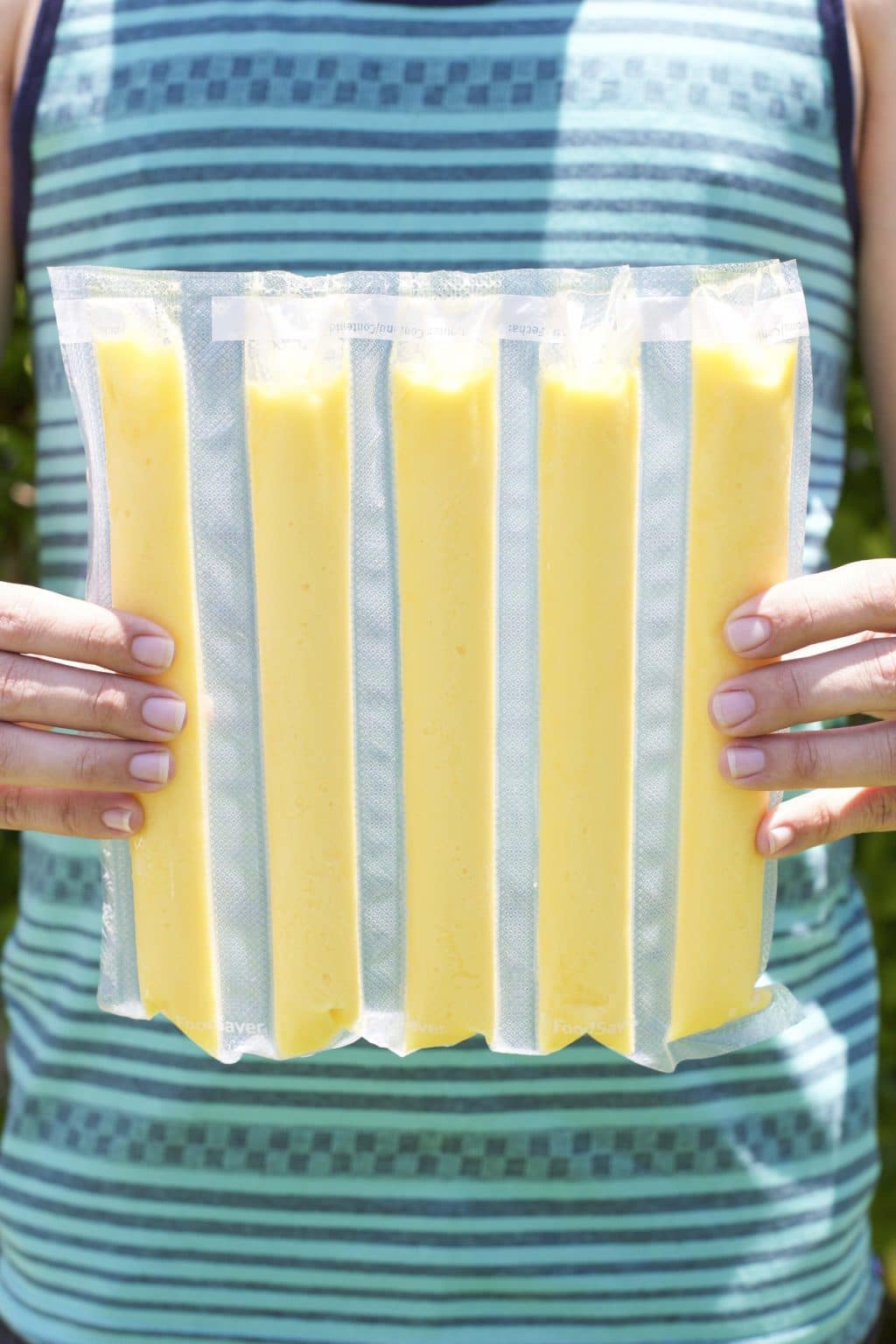 A person holding a bunch of individually wrapped mango popsicles.