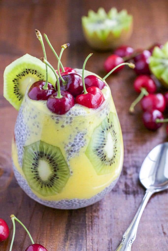 A cup filled with chia seed pudding and fruit on a wooden table top. 