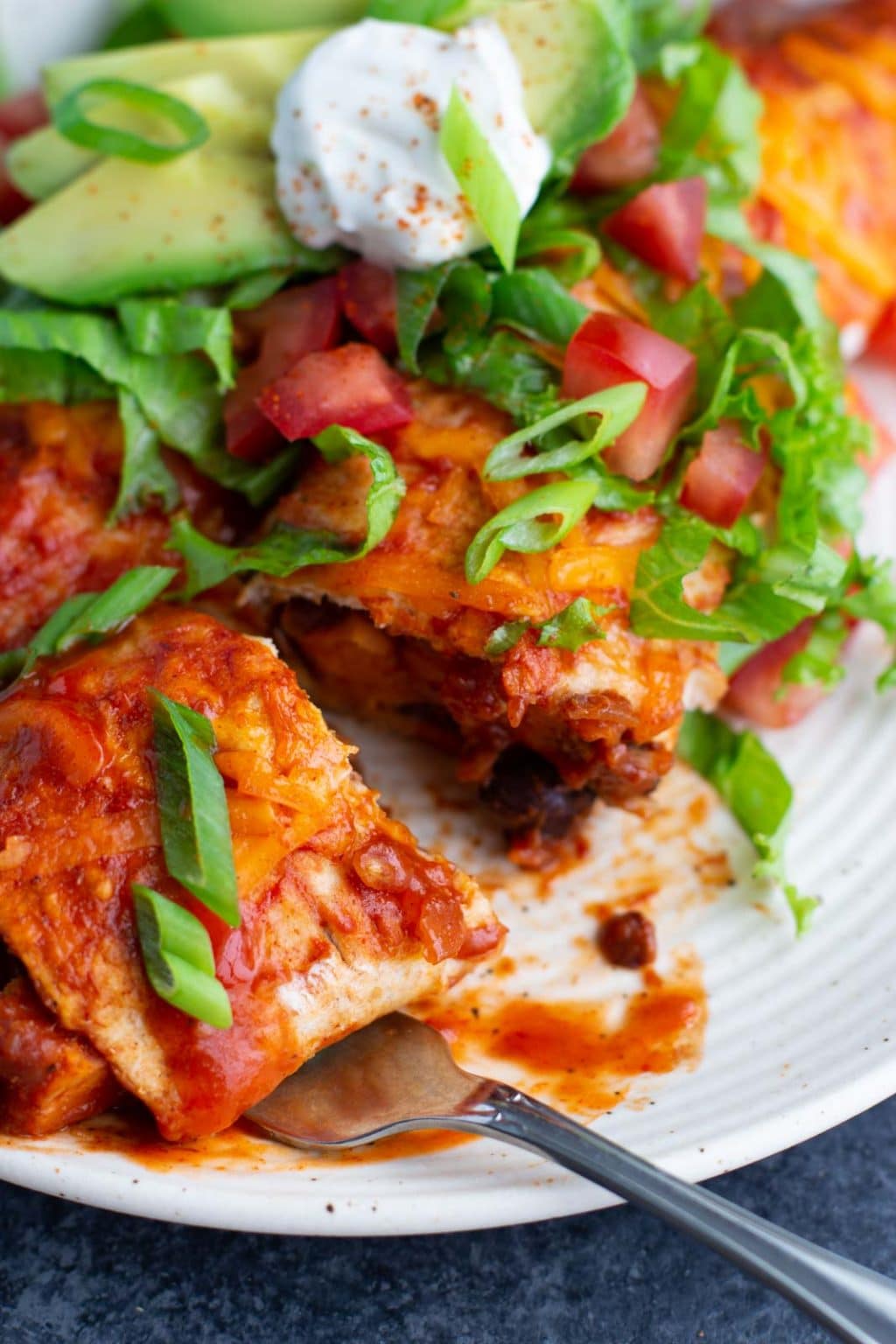 A fork underneath an enchilada that's been cut into on a white plate. 