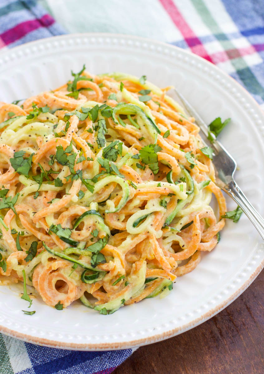 A white plate filled with spiralized vegetable noodles and a fork on top of a plaid napkin. 