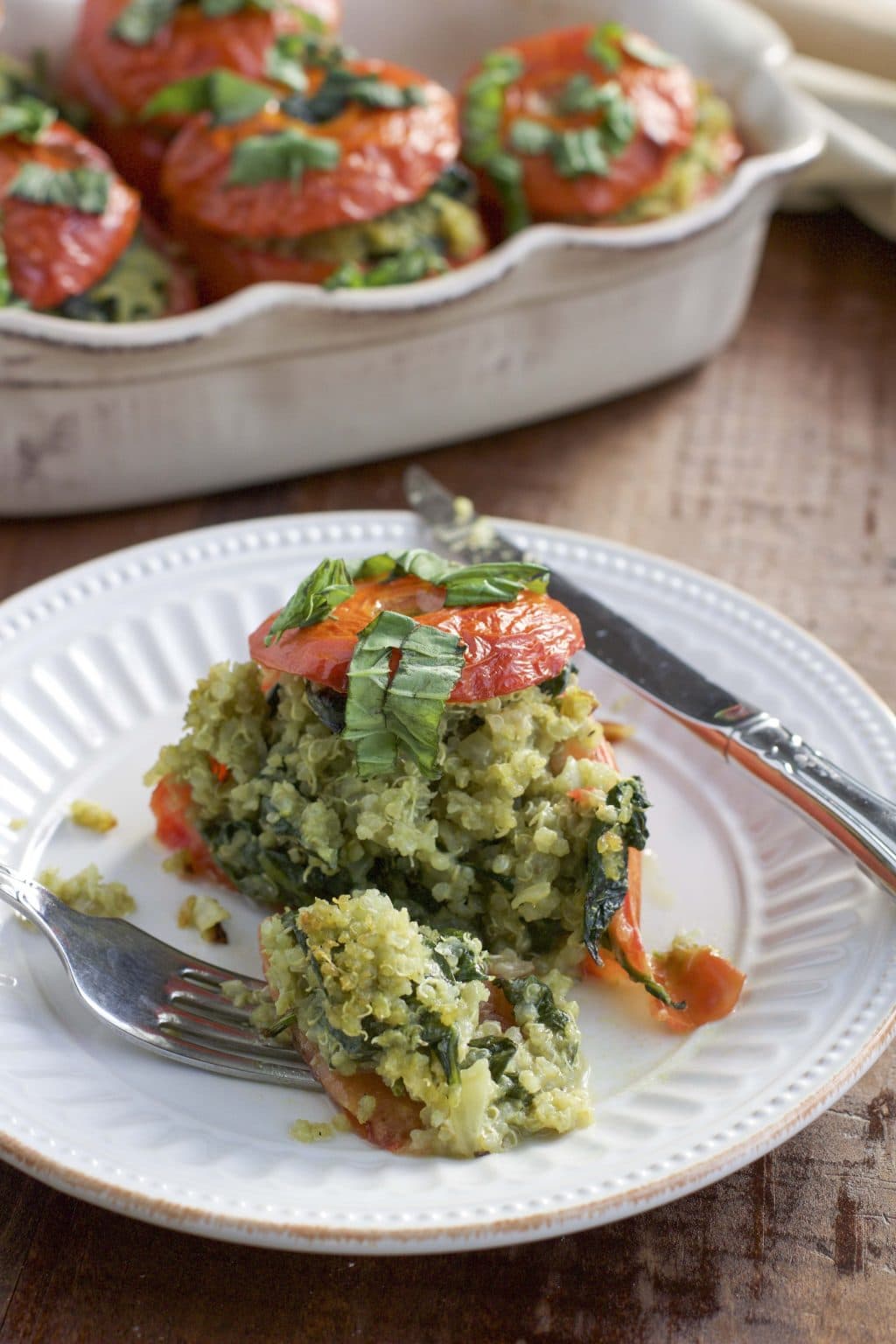 A vegan stuffed tomato cut in half on a white plate with the filling spilling out.