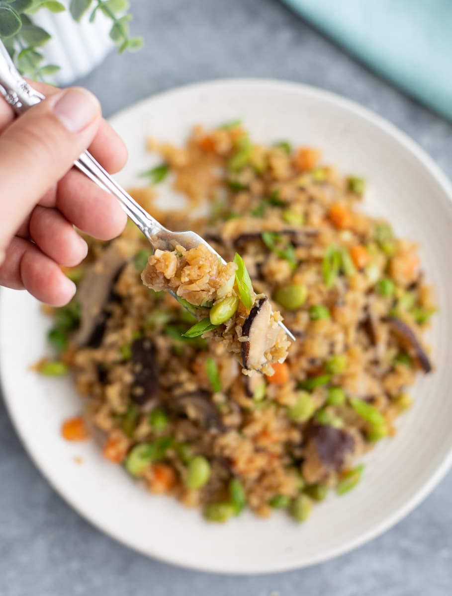 A hand holding a fork over a plate filled with mushroom fried rice. 