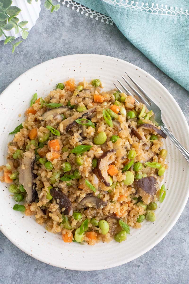 A white plate filled with vegetables and a fork on a gray background. 