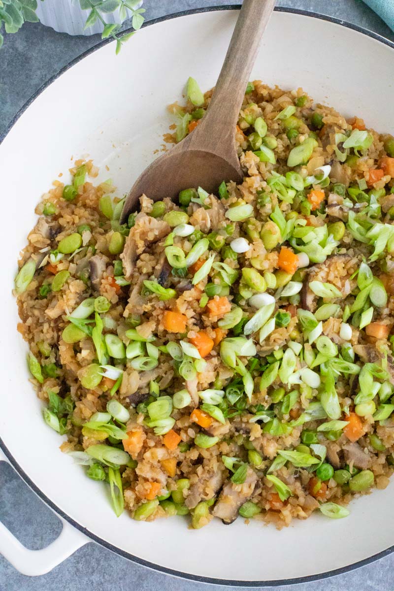 A large white pan filled with vegetables and a wooden spoon on a gray background.