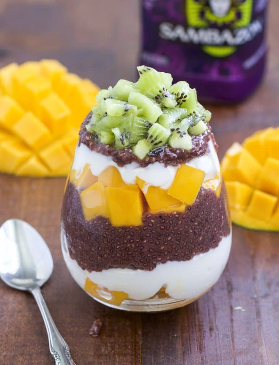 A cup filled with layers of vegan yogurt, chia seed pudding, and fresh mango on a rustic background. 