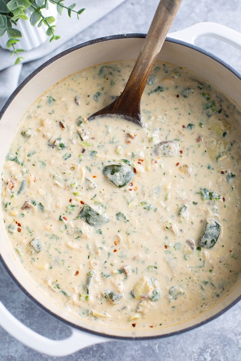 A white pot filled with a creamy soup and a wood spoon on a gray background.