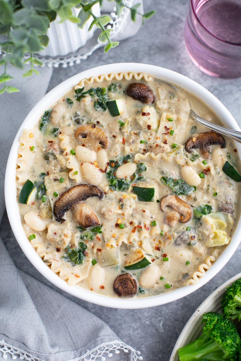 A white bowl filled with lasagna soup and a spoon on a gray background.