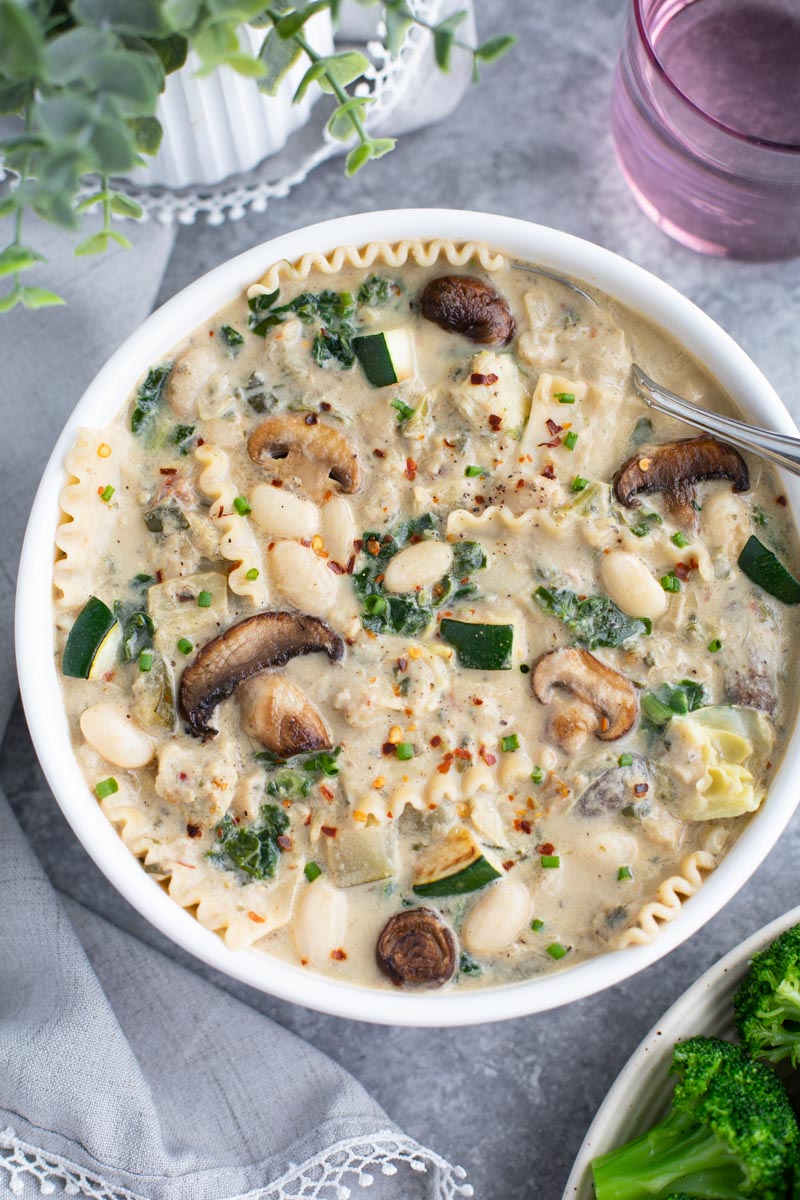 A white bowl filled with lasagna soup and a spoon on a gray background. 