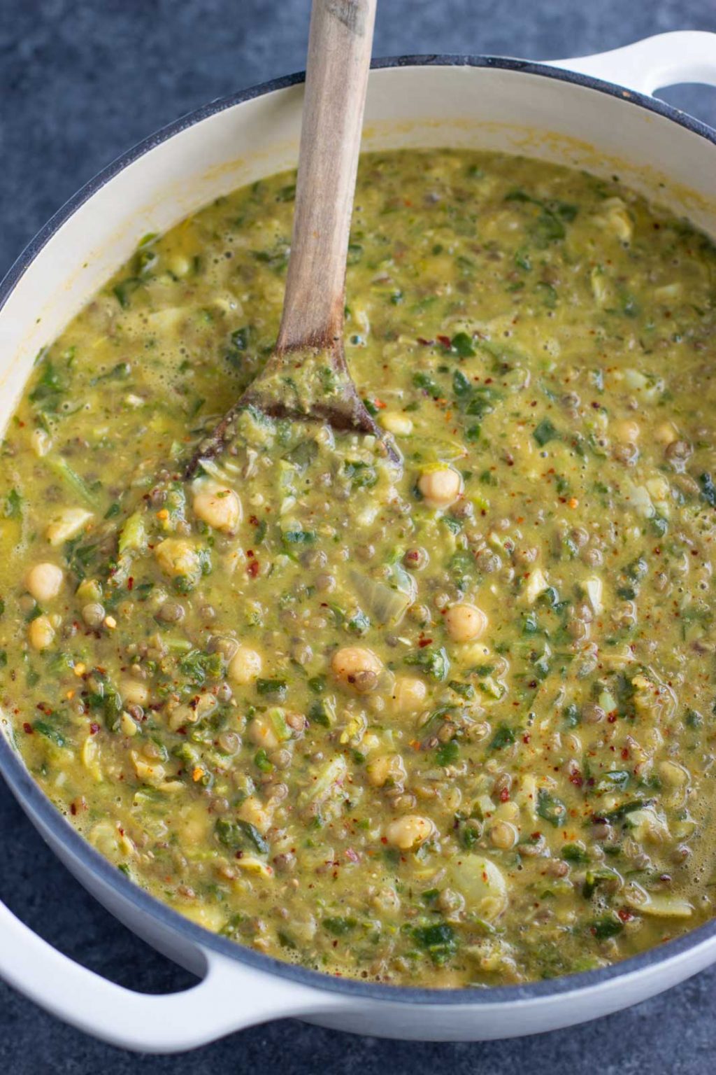 A large pot filled with chickpea soup being stirred with a wooden spoon.