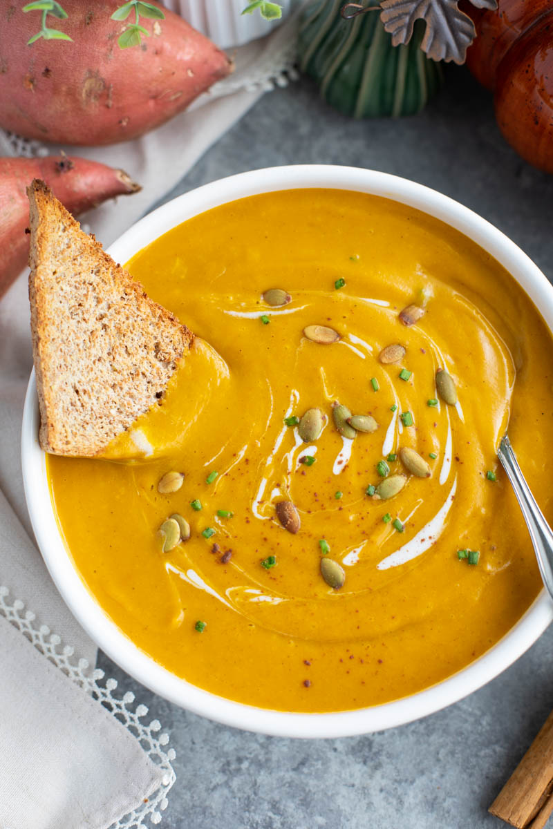 A white bowl filled with vegan pumpkin soup, bread, and a spoon on a gray background. 