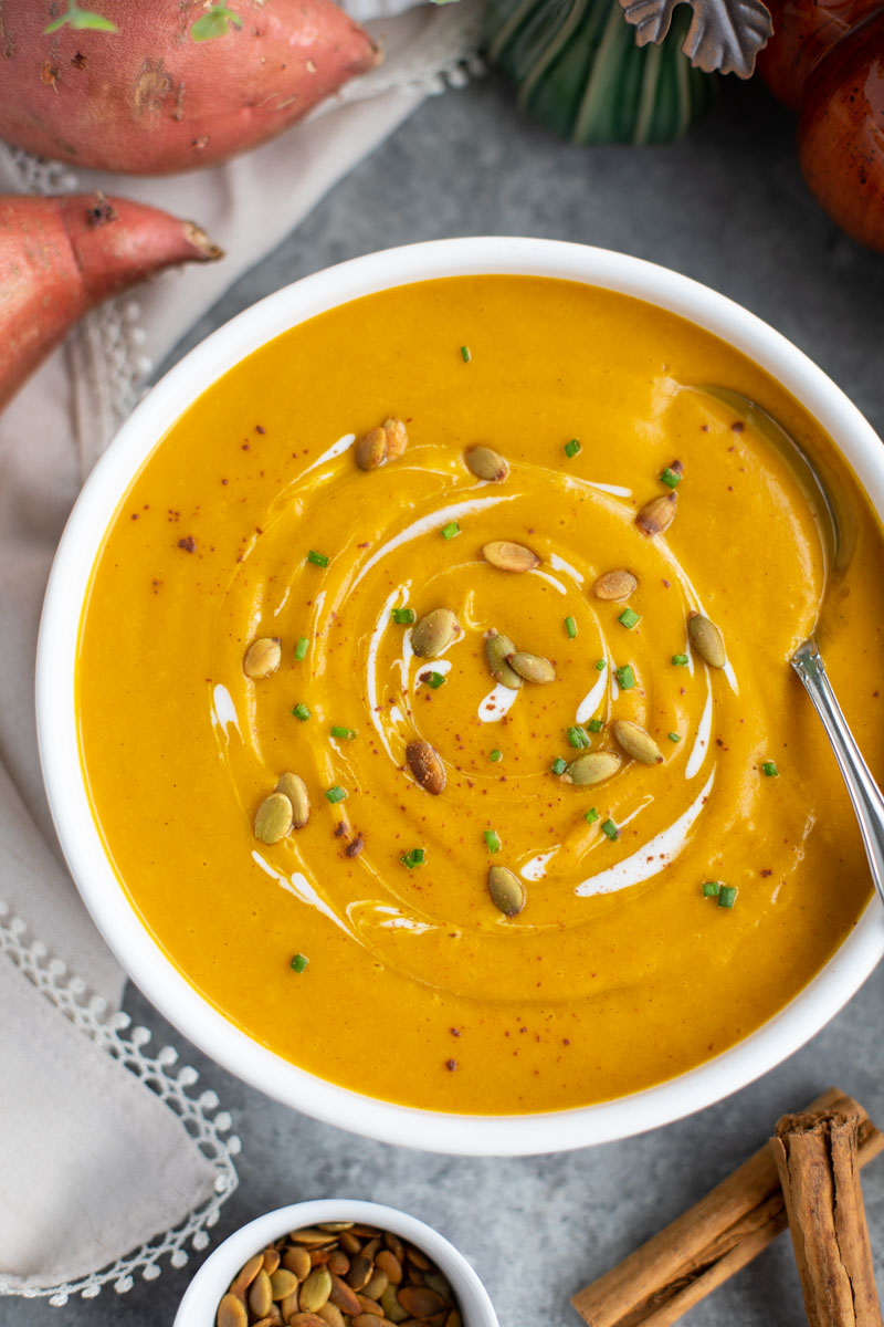 A white bowl filled with pumpkin sweet potato soup and a spoon on a gray background. 