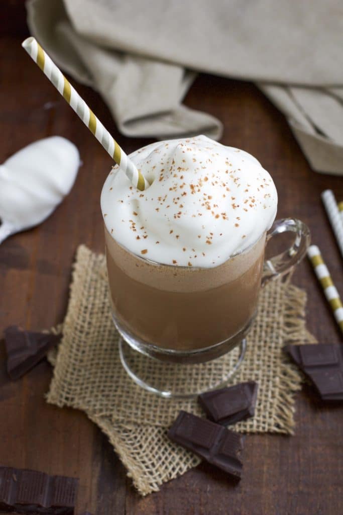 A overhead view of coffee with whipped cream in a glass mug on a rustic background.