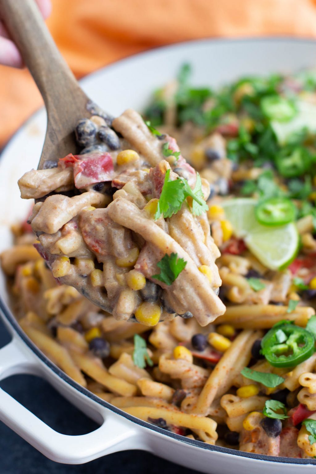 A white skilled filled with taco pasta salad that's being scooped out by a large wooden spoon. 