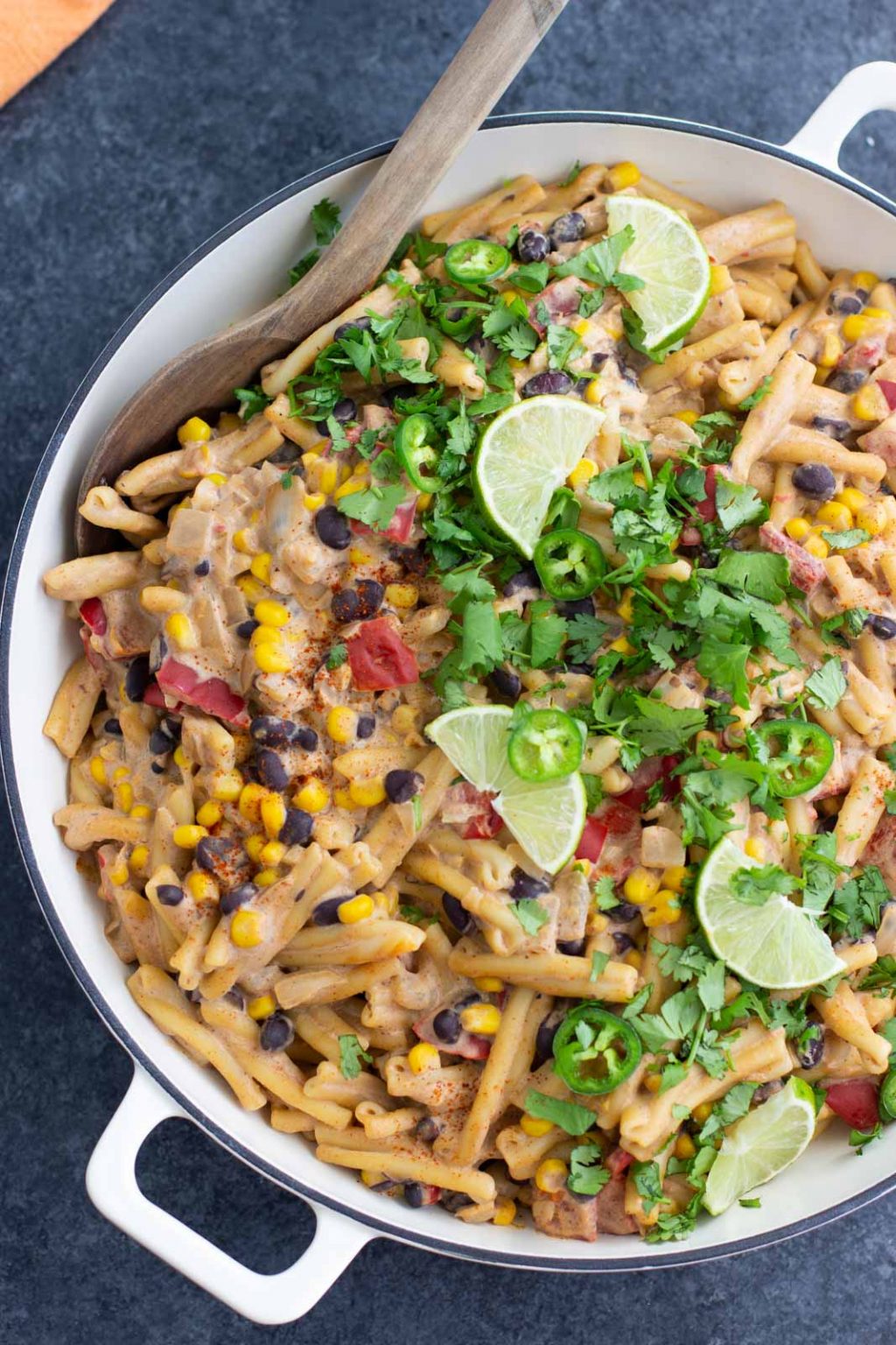 A white pan filled vegan taco pasta and topped with limes, sliced jalapeños, and cilantro. 