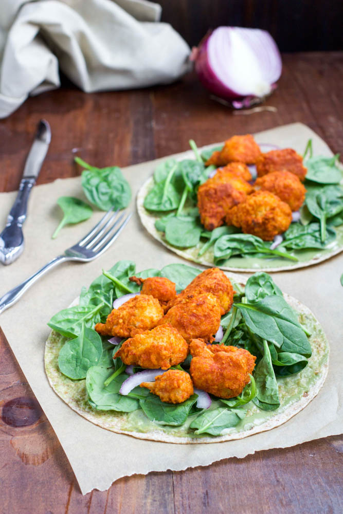 Two open faced wraps laying on top of parchment paper on a wood table. 