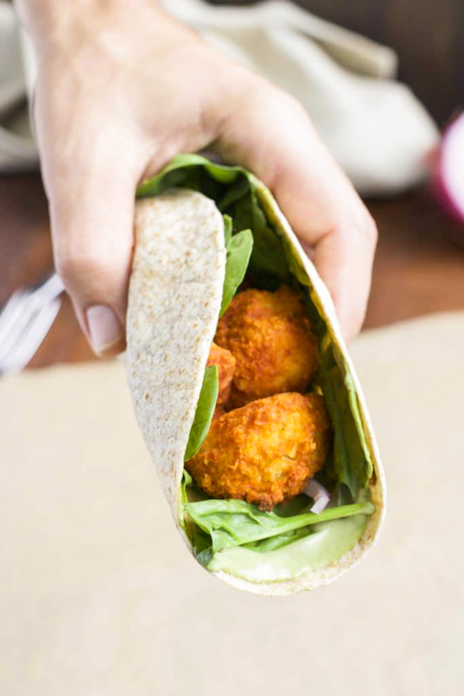 A hand holding a wrap filled with buffalo cauliflower over a piece of parchment paper. 