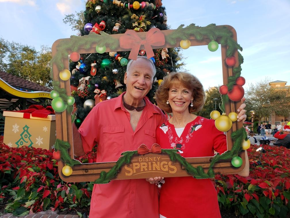 Two people smiling and holding a Disney Springs Christmas photo frame in from of them.