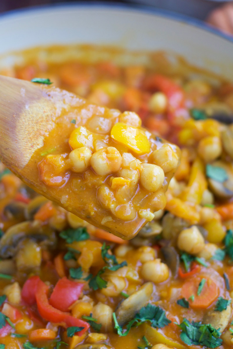 A close up view of saucy chickpeas on a wooden spoon. 