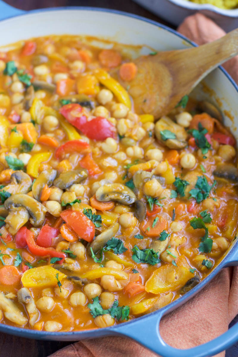 A large blue pan filled with vegetables and a wooden spoon next to an orange napkin.