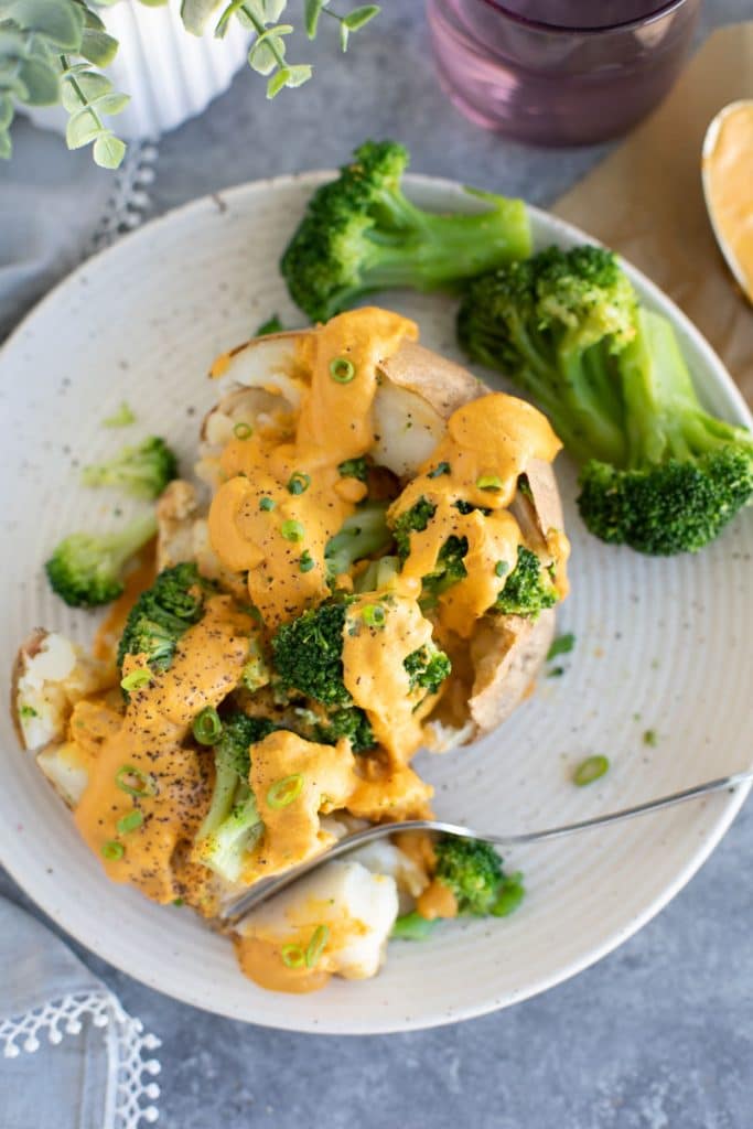 A potato split in half with a fork and topped with broccoli and cheese. 