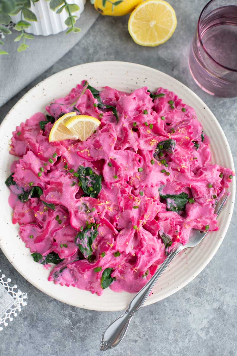 Pink pasta on a white plate next to half a lemon on a gray background.