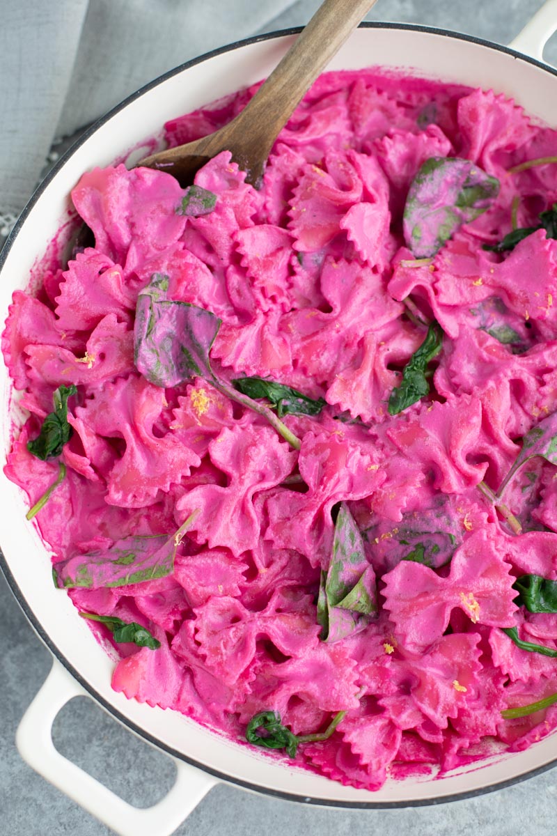 Pink pasta with a wooden spoon in a large white pan on a gray background.