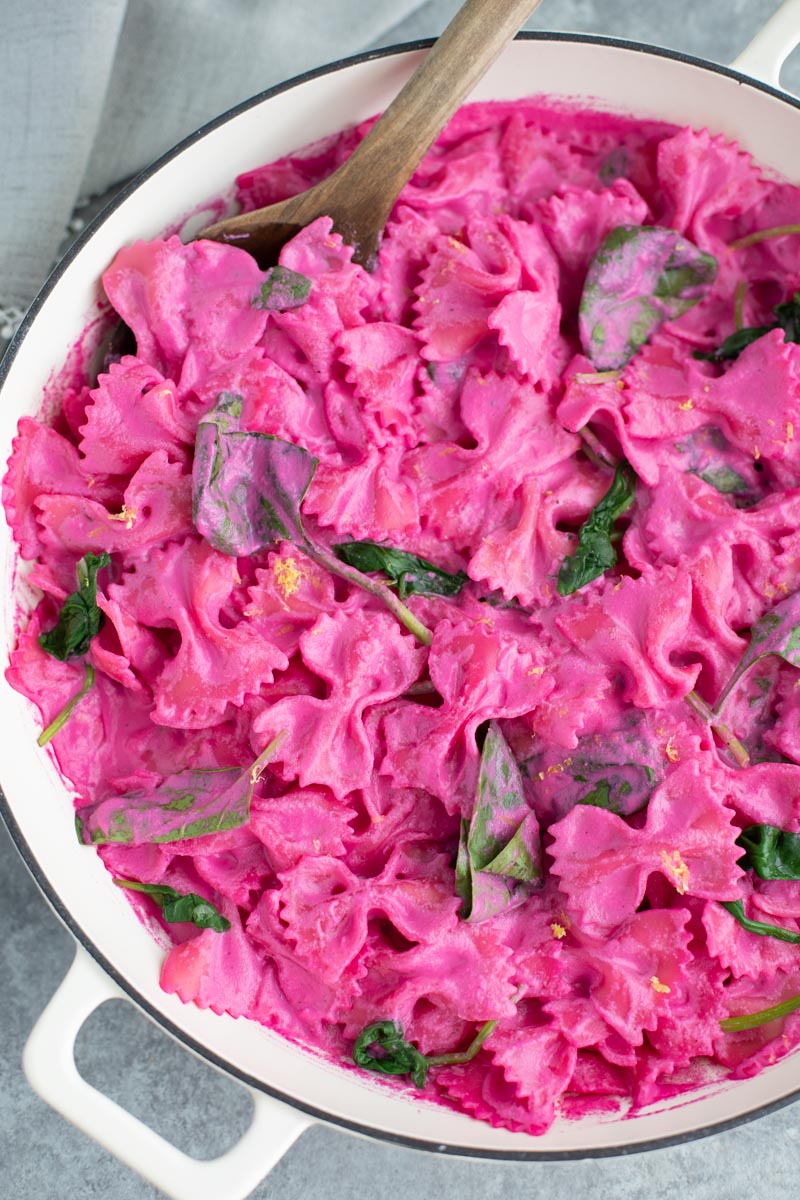 Pink pasta with a wooden spoon in a large white pan on a gray background. 