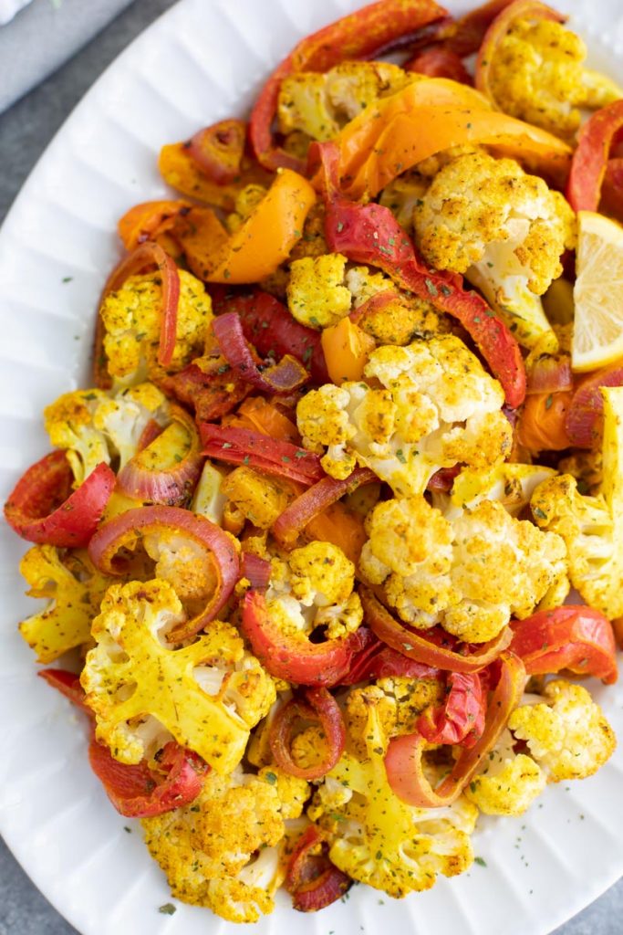 Turmeric roasted cauliflower, peppers, and onions on a large white platter. 