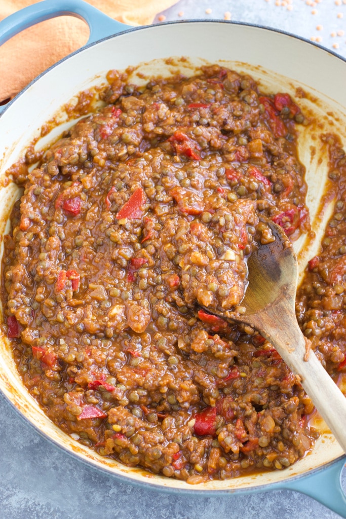 A large pan filled with sloppy joes filling being stirred by a wooden spoon. 