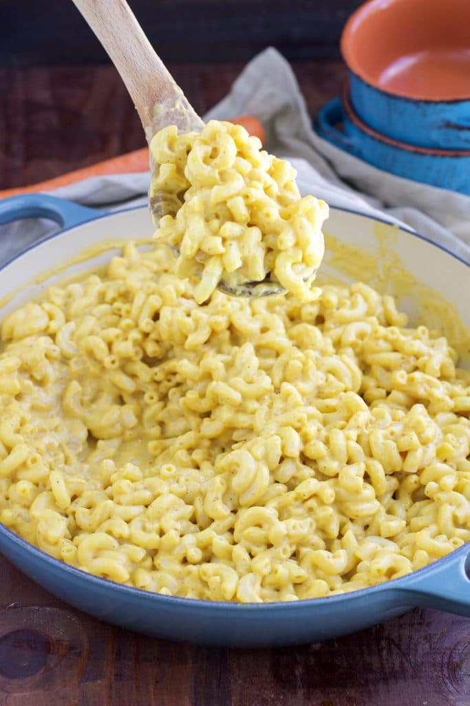 A wooden spoon scooping pasta our of a blue pan on a rustic background. 