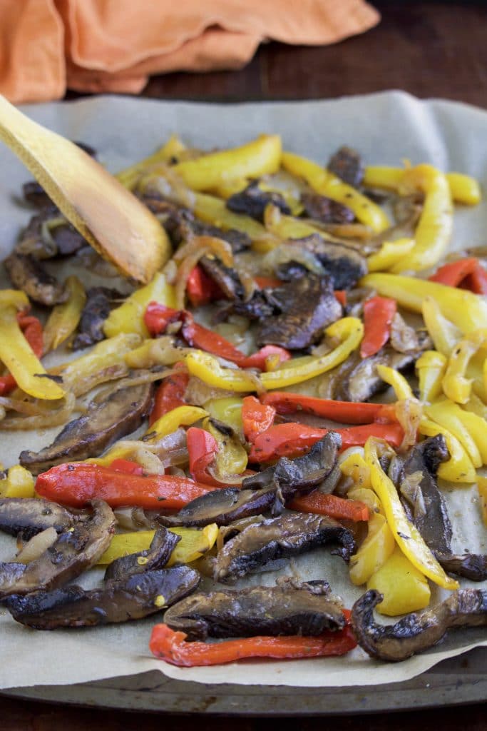 A parchment lined tray filled with roasted slices of portobello mushrooms, bell peppers, and onions. 