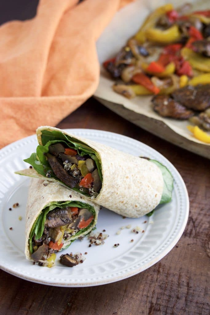 One half of a wrap resting on top of the other half on top of a white plate that's sitting on a rustic background. 