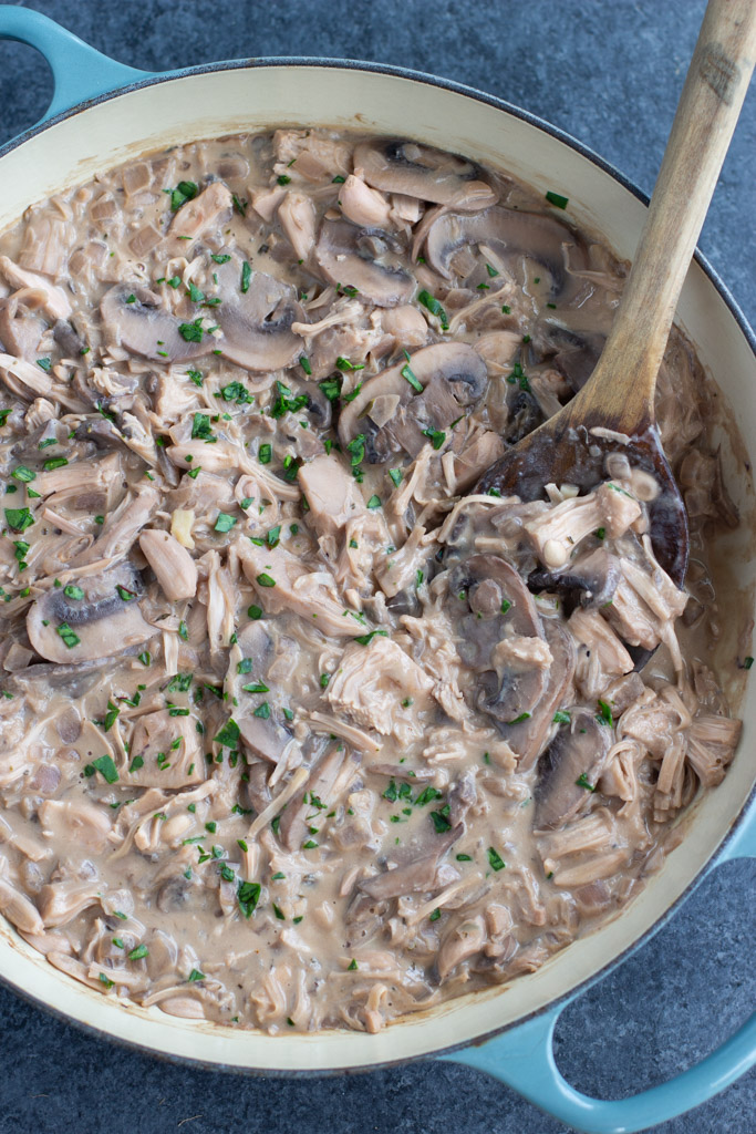 A blue pan filled with food and a wooden spoon on a dark background.