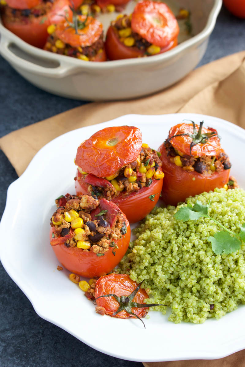 A white plate filled with stuffed tomatoes and a side of cilantro lime quinoa. 