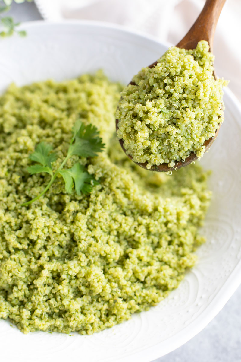 A wooden spoon dipping into a large white bowl filled with quinoa. 