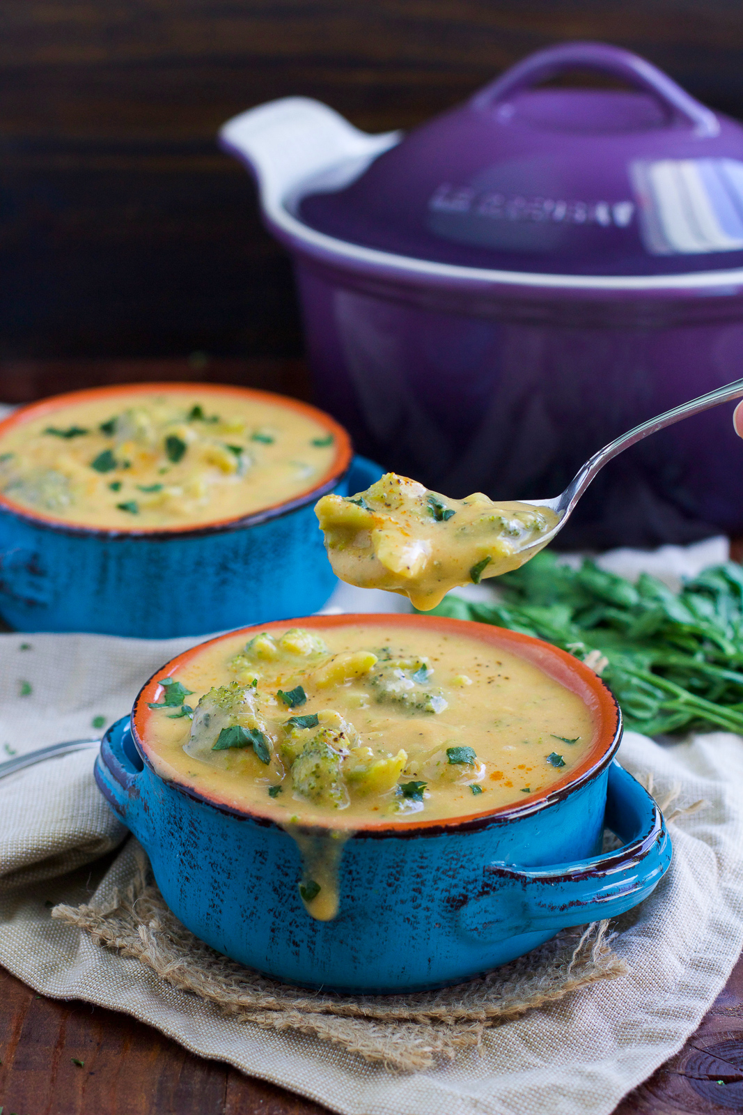 Two blue bowls filled with vegan broccoli cheese soup and a spoon dipped into one of the bowls.