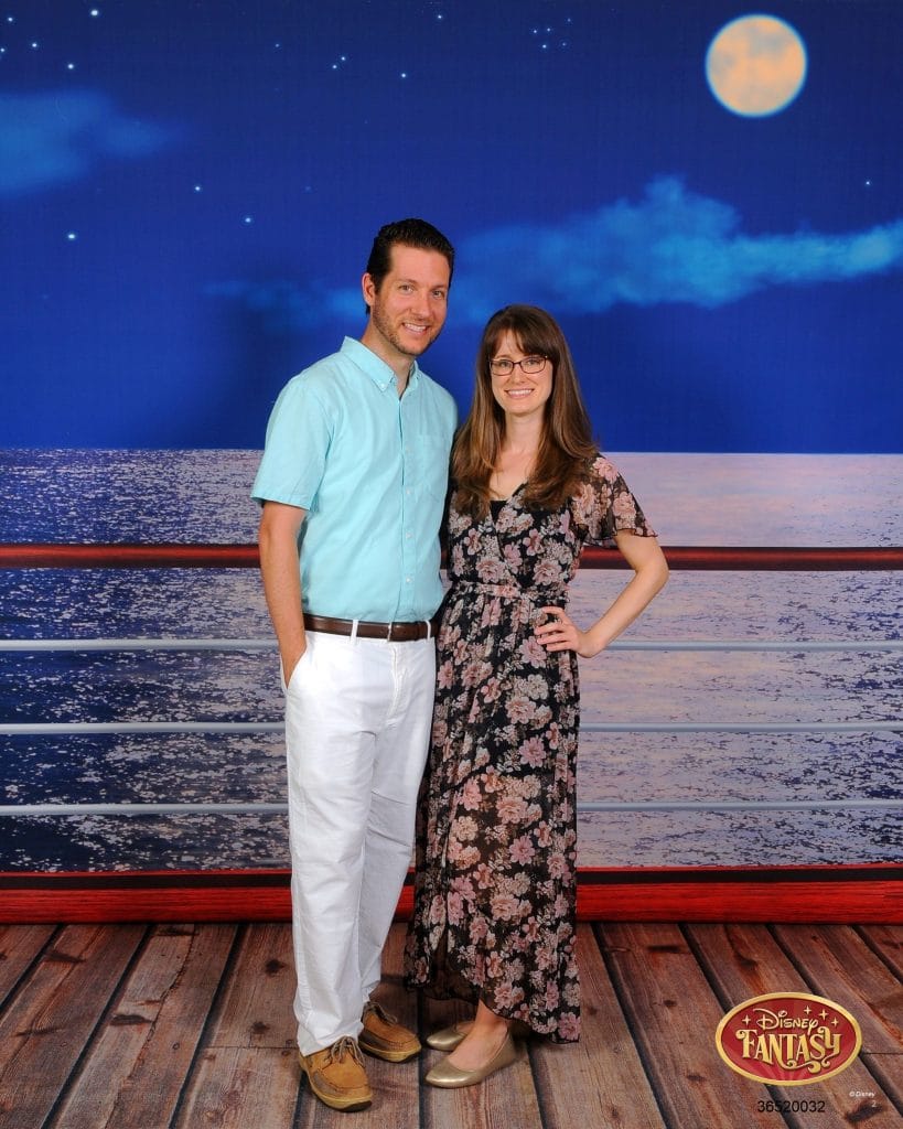 A man and woman smiling and posing in front of the railing at night on the Disney Fantasy.