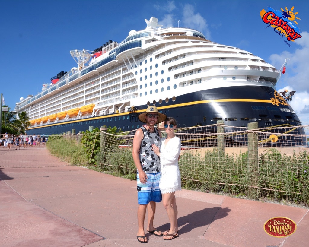 A happy couple posing in front of the Disney Fantasy ship while it's docked at Castaway Cay. 