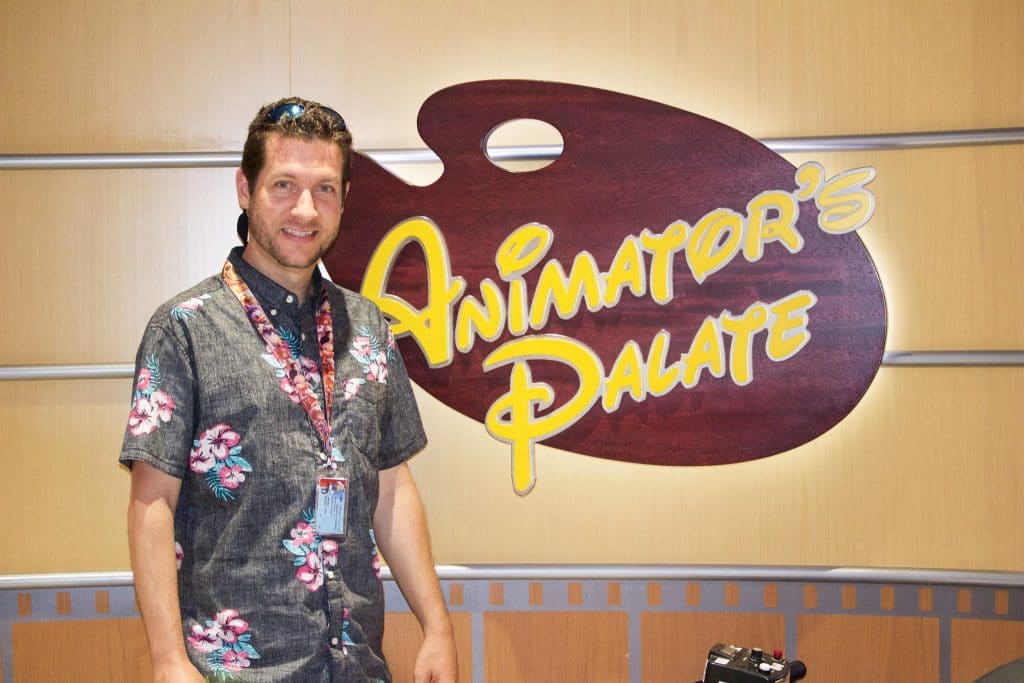 A man standing in front of the Animator's Palate sign on a Disney cruise. 