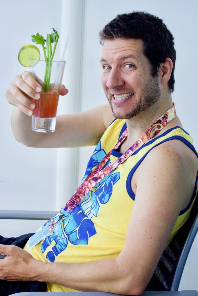 A man in a yellow tank top holding a Bloody Mary.